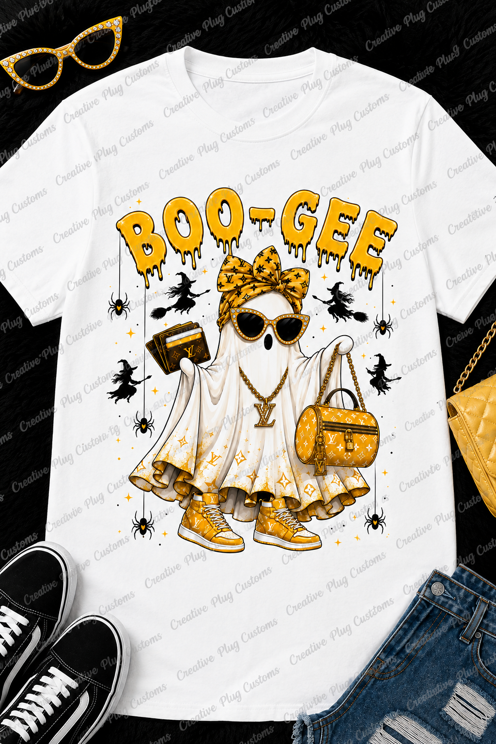 A white graphic t-shirt featuring a Halloween-themed ghost character with a gold monogram pattern, sunglasses, and the text 'BOO-GEE' in yellow dripping letters. The shirt is styled in a flat-lay arrangement with black sneakers, blue jeans, a gold purse, and gold-framed glasses on a black background.