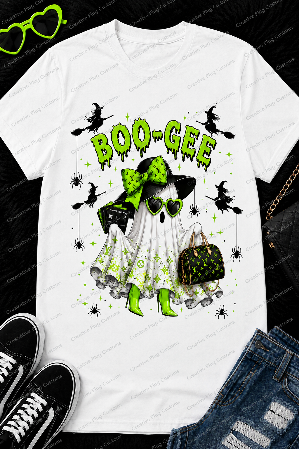 A white graphic t-shirt featuring a Halloween-themed ghost design with green accents, displayed in a flat-lay arrangement with jeans, sneakers, sunglasses, and a purse on a black textured background.